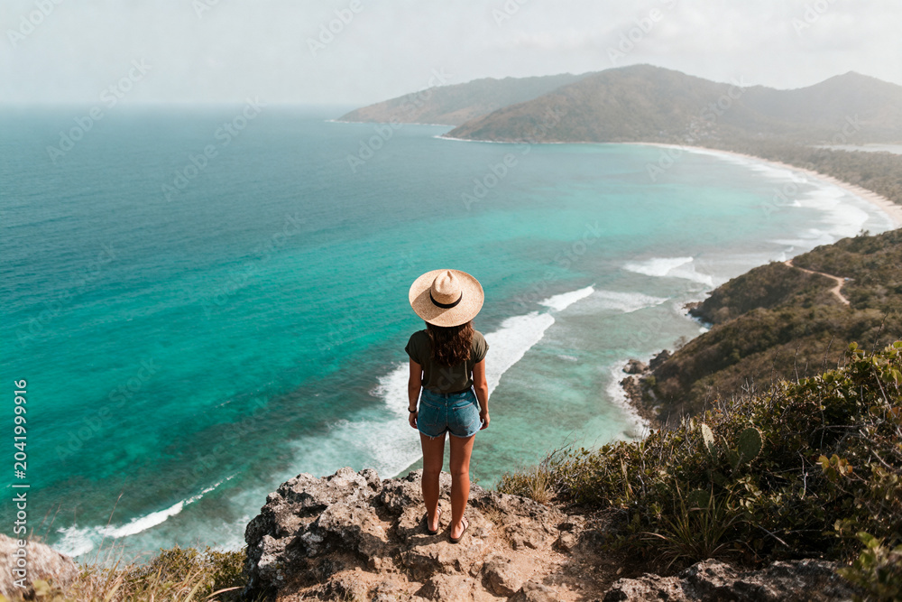 Fototapeta premium Woman standing on cliff overlooking turquoise ocean and coastline
