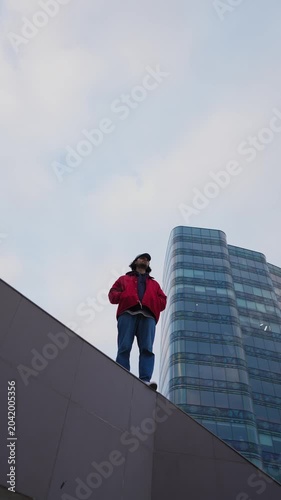 Person standing on edge of urban structure with modern skyscraper in background. Concept of freedom, confidence and urban lifestyle. Vertical video