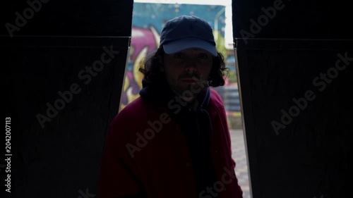 Young man in red jacket walking toward camera in urban street environment. Slow motion video. Concept of youth culture, confidence and city lifestyle
