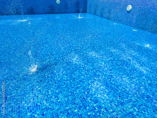 Foto Water splashes arise from the pool floor as sunlight hits the blue tiles during