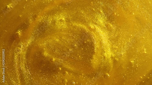 Beautiful abstract golden liquid paint swirl background, beauty gold backdrop texture. Metallic gold paint, art design. Yellow shimmering surface closeup. Golden bright glitter texture. Rotating 
