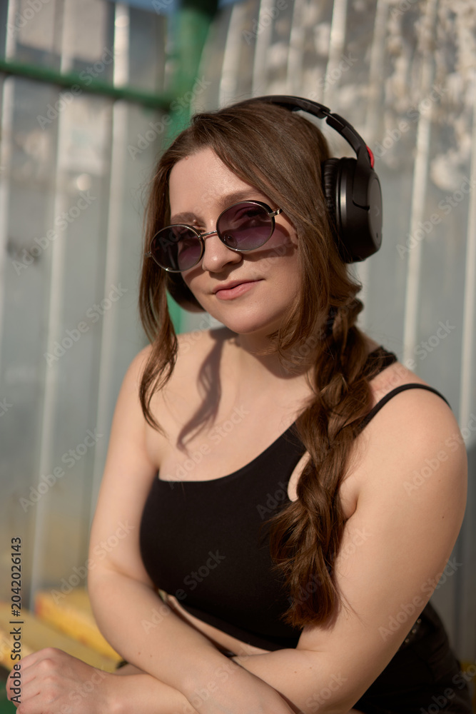 Fototapeta premium Woman enjoying a sunny day with headphones, sunglasses, and a playful spirit in a vibrant outdoor setting