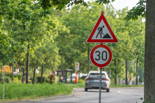 Fotografie A roadworks warning sign stands above a thirty speed limit sign