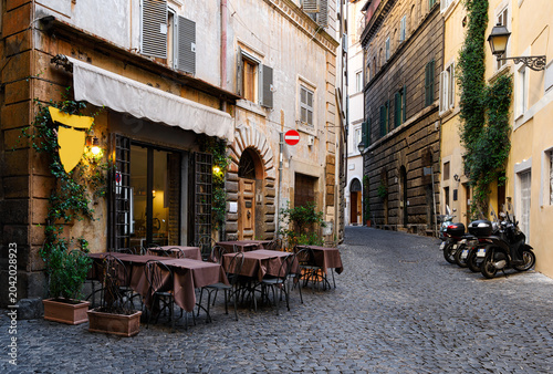 View of old narrow street with tables of restaurant in Rome, Italy. Architecture and landmark of Rome. Cozy cityscape of Rome.