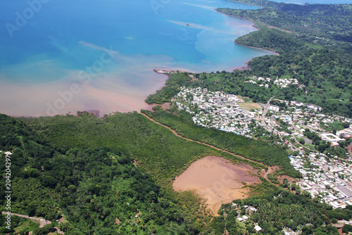 Vue aérienne d'une ville côtière de Mayotte bordée de mangrove et d'eaux sédimentaires colorées