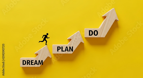 Hand arranging wooden blocks with dream plan do goals on bright yellow background