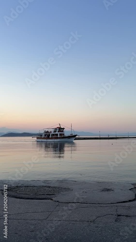 Fishing boat entering a harbor at sunset on a Greek island, calm glassy sea, golden reflections on the water, peaceful Mediterranean atmosphere, cinematic travel video