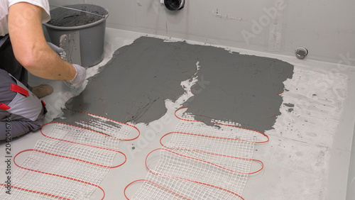 Electric Heating Mat Installing in the Tile Adhesive. Underfloor Dual Core Fiberglass Mesh Mat. Warm Floor Heating System. Warming. Worker Applying Concrete Mortar for Warm Floor. Renovation work. 4K