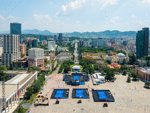 Aerial view of Skanderbeg Square featuring temporary tennis courts surrounded by historic buildings and modern skyscrapers under a clear sky in Tirane, Tirana County, Albania.