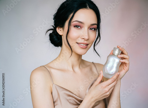 A beautiful sexy lady in an elegant nude bodysuit holds a bottle in her hands. Fashion beauty portrait of fashion model