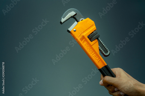 Photography Plumber hand holding handle of chrome pipe wrench isolated on dark background
