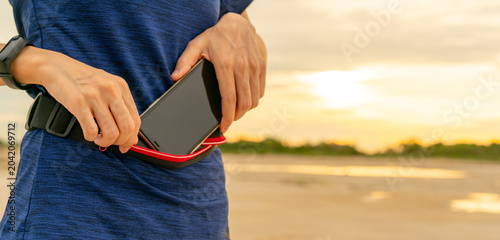 Foto Young Asian woman keep smartphone in waist bag before running cardio exercise in the morning