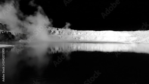 Black and white view of a misty geothermal lake with cliffside reflected on the water's surface, Iceland