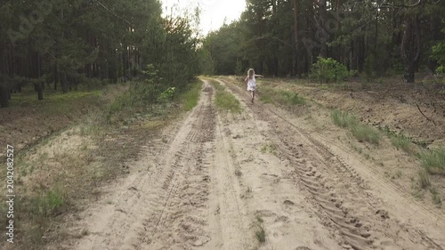 Two little sisters have fun run along country's lean of sandy road among pine boron.