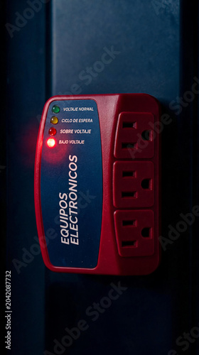 Protector de voltaje para equipos electrónicos con luz indicadora de bajo voltaje encendida. Concepto de seguridad eléctrica, fallas de energía y protección de electrodomésticos.
