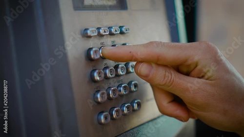 Dialing number on vintage public payphone with metal keypad in urban street environment. Closeup finger pressing old telephone booth buttons during outdoor communication call. Retro telecommunications