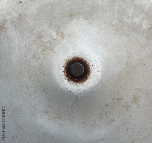 Rusty bolt in center of scratched aluminum metal surface