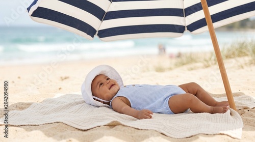 Baby relaxing under sun umbrella on sandy beach by the ocean  