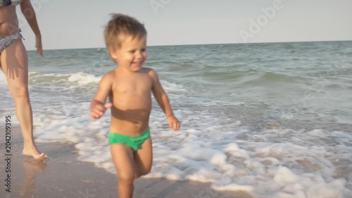 A girl in a swimsuit runs with a toddler on the beach with shells on the background of the sea with waves