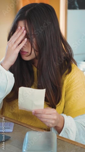 Video of a young Hispanic woman frustrated while doing calculations with her calculator to pay her debts. Concept of economic problems in everyday life, household expenses, and personal debt.

