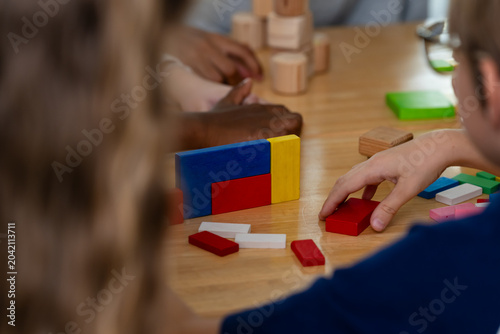 Close group view of young pupils arranging colorful block during back to school elementary classroom activity, wooden tower on desk, cooperation, logic, creativity, peer learning skill develop