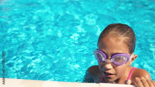 A girl in a pink bathing suit in purple glasses floats on a pool with blue water on a summer day