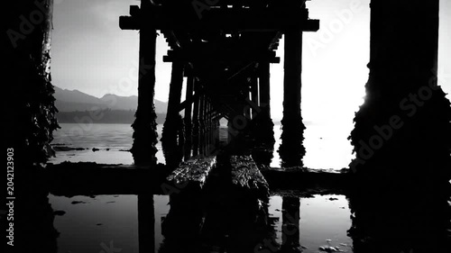 Low angle shot of a wooden pier over water with mountain silhouette in the background, monochrome
