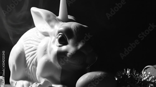 Black and white close up of a white ceramic rabbit figurine with a candle and festive decorations