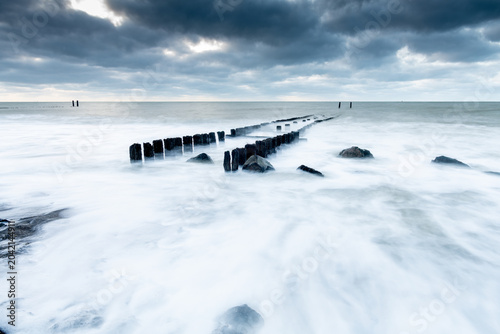 Moody Coastal Landscape in Westkapelle, The Netherlands with Wooden Groynes and Soft White Water Under Overcast Sky