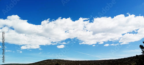Beautiful cloudy blue sky background. Light blue sky with small fluffy white clouds. A calm and clear atmosphere. Space for text layer background design. Panorama of a cloudy sky on a sunny day.