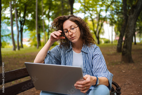 Woman working on laptop outdoors in park with trees