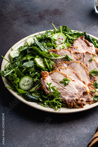 Slices of pork meat roast served with green vegetables salad in plate
