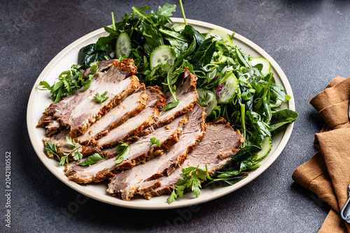Slices of pork meat roast served with green vegetables salad in plate