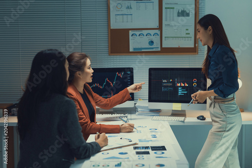 Business women collaborating and analyzing financial charts on computer screens, discussing strategy and marketing reports in the office