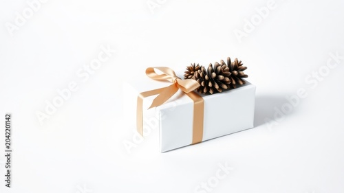 A pristine white gift box adorned with a delicate gold ribbon and natural pine cones