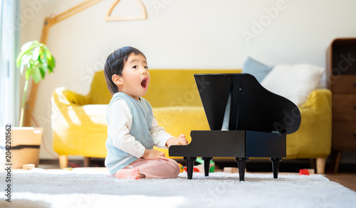 Bild auf Leinwand リビングでおもちゃのピアノを弾く3歳の男の子