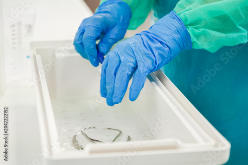 A medical professional wearing blue gloves cleans surgical instruments in a sterile liquid basin, ensuring high hygiene standards within a clinical hospital operating room setting