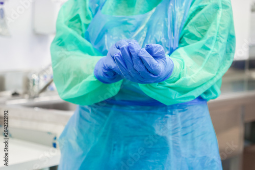 A medical professional puts on blue nitrile gloves in a clinic while wearing a protective gown to prepare for a clinical procedure ensuring safety and hygiene in a healthcare setting