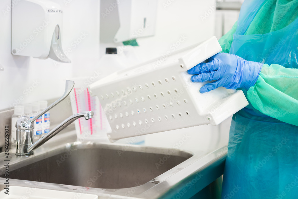 Naklejka premium A gloved worker sanitizing a plastic basket at a sink in a medical facility to emphasize the strict hygiene protocols and cleaning procedures required for a sterile environment