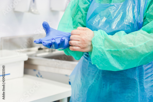 Photography A medical professional wearing a blue surgical gown puts on protective nitrile g