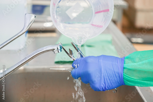 Принти на полотні A gloved hand rinses surgical metal instruments with clean water from a measurin