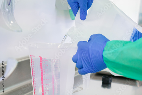 Photos A laboratory technician wearing blue protective gloves pours clear liquid from a