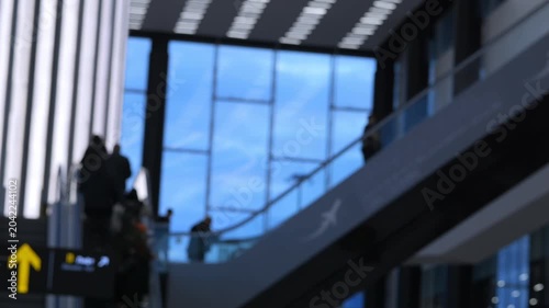 Modern airport interior with blurred travelers on escalators. People move quietly, focused on their journey. Blurred background highlights architectural design. Ideal for travel, transit