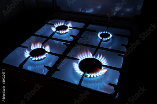 Four blue propane gas burners burning simultaneously on a kitchen stove range in the dark. kitchen cooking appliance