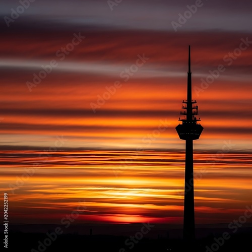 Tower silhouette against fiery horizon streaked with vibrant sunset clouds