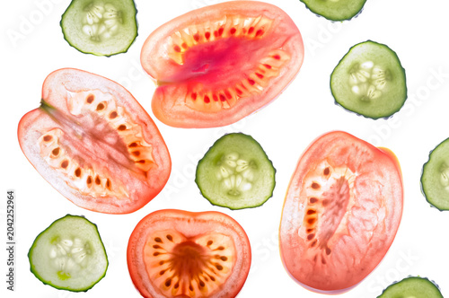 Backlit thin slices of fresh red tomatoes and green cucumbers revealing translucent cellular texture and seeds