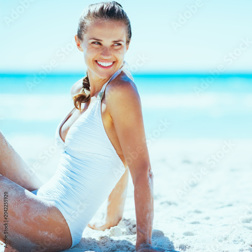 Smiling young woman sitting on beach and looking on copy space