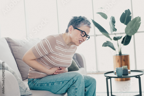 Cuadro en lienzo Senior woman clutching stomach in pain while sitting on sofa at home, experienci