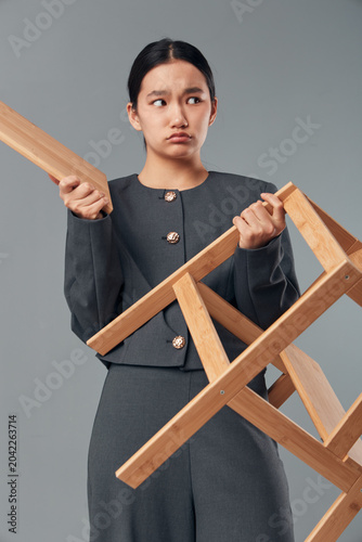 Canvas-taulu Young woman holding wooden chair with unhappy expression in studio