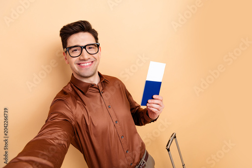 Quadro em tela Smiling young man holding passport and boarding pass for travel selfie with carr